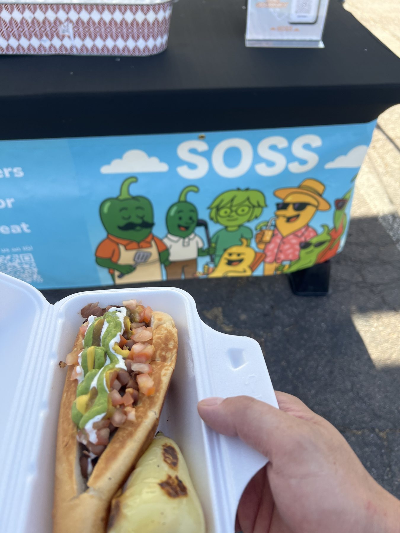 A taco topped with SOSS in front of the market booth